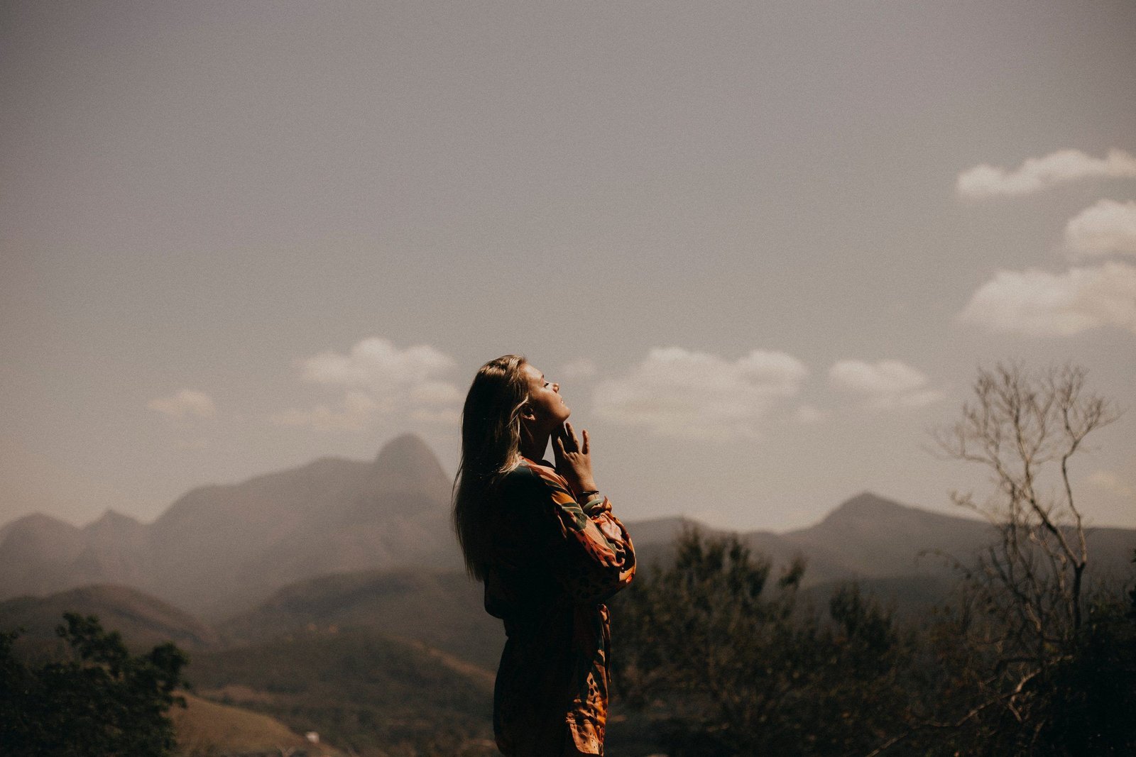 A woman standing before a mountain range, face lifted to the light
